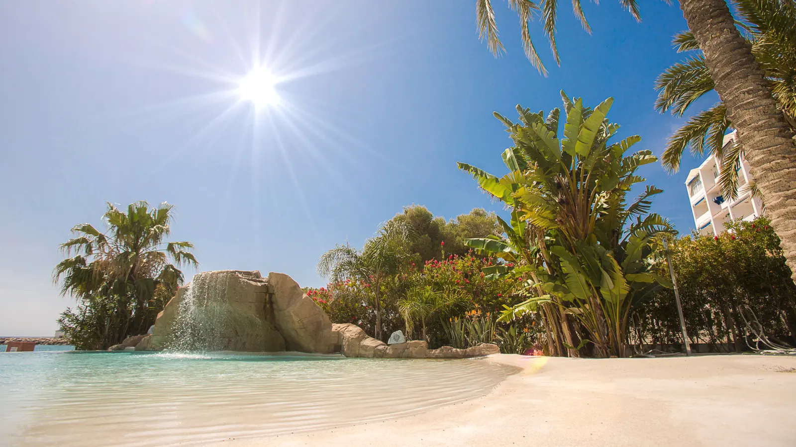 Piscina de arena con playa de acceso y cascada bajo el sol